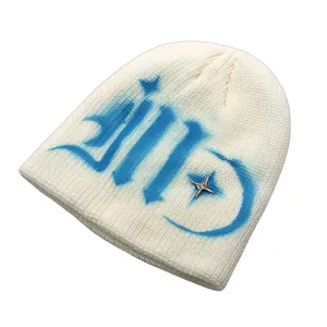 Detail of cream knit beanie with blue graffiti print and silver star charm accessory