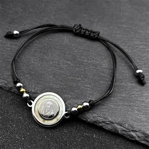 Handmade woven Saint Benedict rope bracelet with gold and silver beads on a stone surface