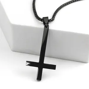 Vue macro d'un pendentif croix inversée noir poli avec chaîne à billes sur socle blanc