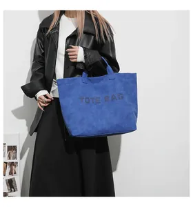 Detail of the blue suede texture tote bag featuring black embossed TOTE BAG lettering