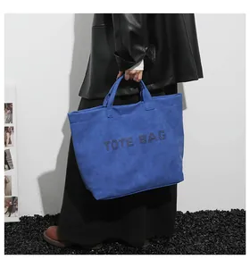 Detail of blue suede tote bag featuring rivet TOTE BAG lettering and double handles