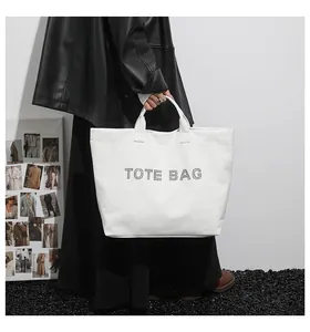 Close-up of a stylish white tote bag featuring black TOTE BAG studded lettering and sturdy handles