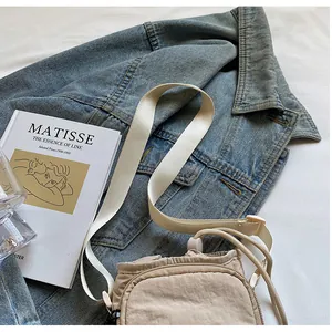 Beige Umhängetasche aus Nylon mit Kordelzug auf Jeansjacke und Kunstbuch liegend