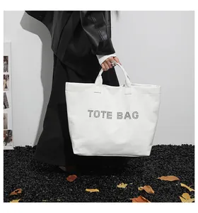 Detail of white tote bag with black lettering held by a model in minimalist studio