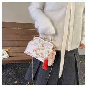 Détail du sac en soie rose avec broderie de baies et pompon rouge élégant sur le côté