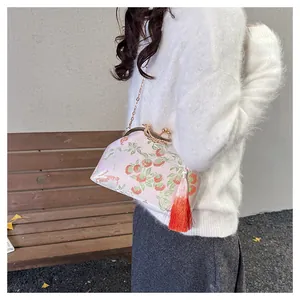 Détail du sac brodé rose avec motifs de kaki et un gland décoratif en soie rouge