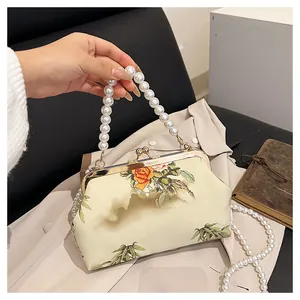 Detail of vintage floral embroidery on cream clutch bag with oversized pearl chain strap