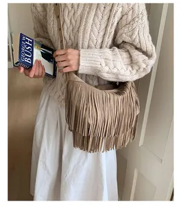 Close-up of khaki suede crossbody bag with long bohemian fringe worn with a white sweater