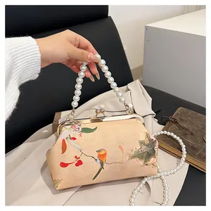 Detail view of floral embroidery on a vintage handbag with pearl handle and golden clasp
