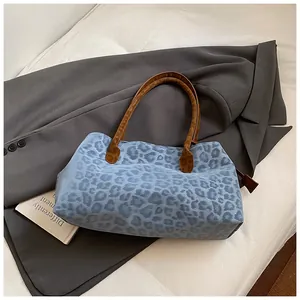 Détail d'un sac cabas à imprimé léopard bleu clair avec anses en cuir marron sur un blazer