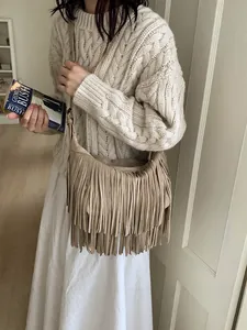 Bohemian beige tassel crossbody bag with suede texture shown in a lifestyle pose