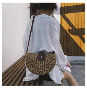 Dettaglio di una borsa a tracolla in paglia intrecciata con patta in pelle su modella