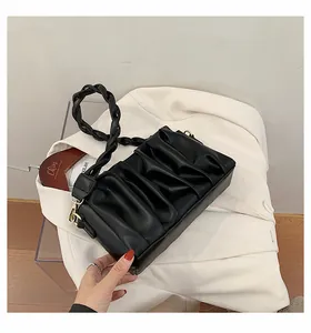 Detailed view of black pleated PU cloud bag with gold hardware on a white blazer