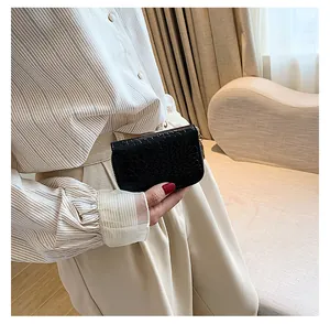 Détail du portefeuille noir texture crocodile avec zip doré tenu par un mannequin en beige