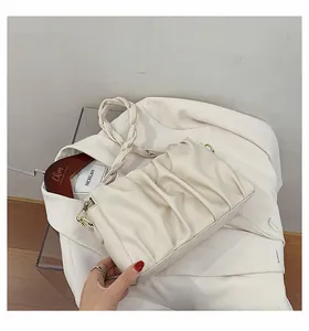 Close-up of beige ruched dumpling bag featuring a braided strap and gold metal hardware