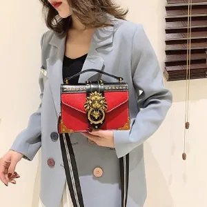 Detailed view of red and black leather crossbody bag with golden lion buckle and rivets
