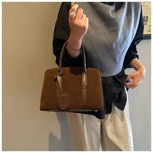 Detail van vintage bruine suède handtas met lederen biezen en metalen beschermvoetjes