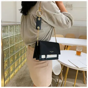 Sac à bandoulière monochrome chic avec chaîne porté par un mannequin dans un café