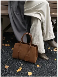 Detailweergave van een bruine suède tas met lederen bies op grind en herfstbladeren