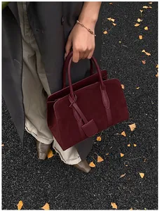 Detail van bordeauxrode suède shopper op herfstbladeren met glad leren accenten
