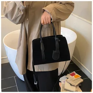 Detail van zwarte suède shopper met lederen hanger, getoond bij een beige trenchcoat