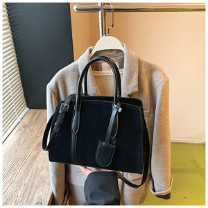 Detail van zwarte suède handtas met stevige handvatten en ronde lederen hanger erop