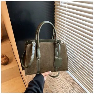 Detail van vintage suède handtas met olijfgroene panelen en een leren schouderband