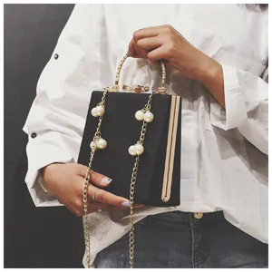Close-up of elegant black box bag with pearl chain and golden bow clasp detail