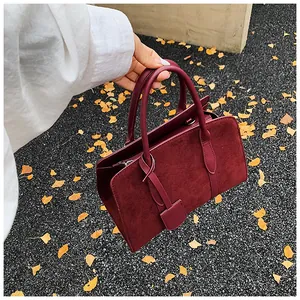 Detail van bordeauxrode suède handtas met lederen hengsels op herfstige achtergrond