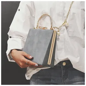 Detail of grey square handbag featuring golden arch handle and pearl chain strap