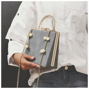 Model showing gray suede box bag with gold handles, bow buckle and pearl chain strap