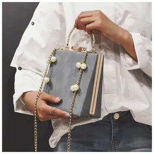 Detail of grey square box handbag with golden metal handle and white pearl chain strap