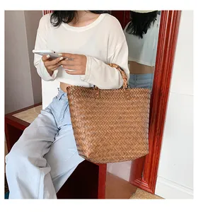 Detail of woven brown tote bag with bamboo handle held by model in casual outfit