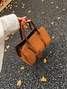 Vintage bruine suède handtas met lederen riemen tegen een herfstige ginkgo blad achtergrond