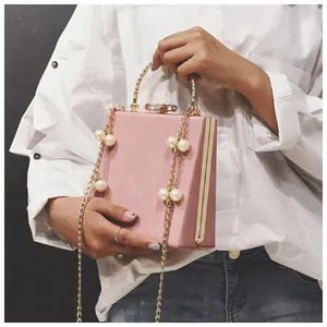 Close-up of pink suede crossbody bag featuring a crystal bow clasp and pearl chain strap