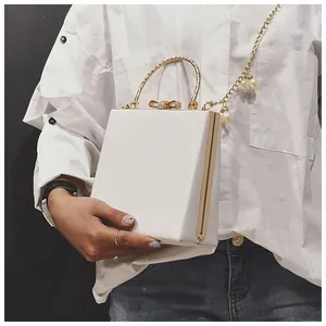 Detail of white box bag with gold metal handle and luxury pearl chain strap detail