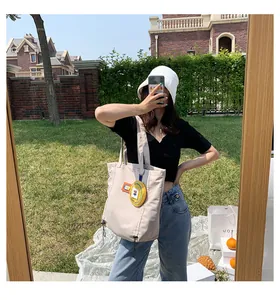 Detail of beige canvas tote bag with yellow purse charm and drawstring side accents