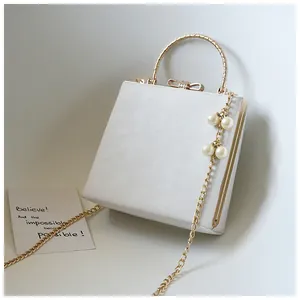 Detail of white evening bag with golden ring handle, pearl charm and bow clasp