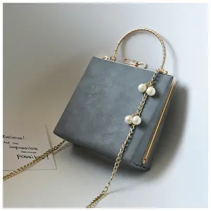 Detail of grey square crossbody bag with gold round handle and pearl chain accessory