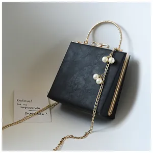 Detail of black square evening bag with gold trim, ring handle and pearl chain charm