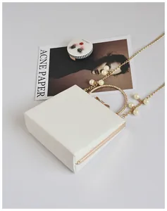 Detail of white square clutch bag with golden ring handle and pearl chain strap