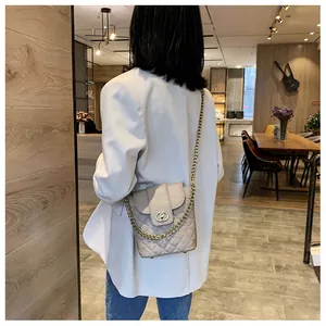 Quilted beige bucket bag with gold chain strap shown on model in a stylish cafe setting