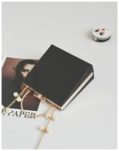 Detail of black square evening clutch with golden bow clasp and pearl chain handle