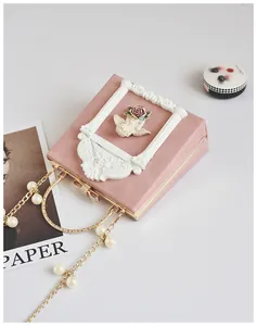 Detail of pink vintage box bag featuring angel relief, gold chain, and white pearl strap