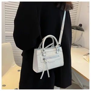 Detail of white crocodile pattern crossbody bag with silver zippers and long leather tassels