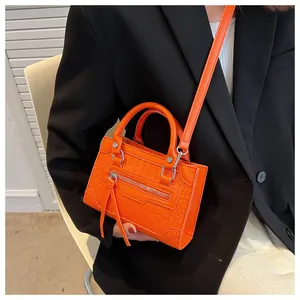 Detail of bright orange crocodile embossed crossbody bag with tassels and silver hardware