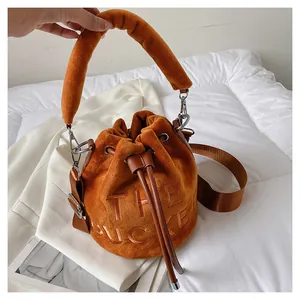 Detail of caramel plush bucket bag with embossed The Bucket text and drawstring closure