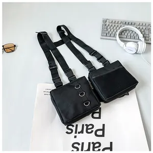 Detail of black tactical chest rig with dual pockets and metal D-rings on grey surface