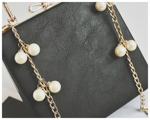 Close-up of black litchi grain leather bag with gold bow and pearl chain detail