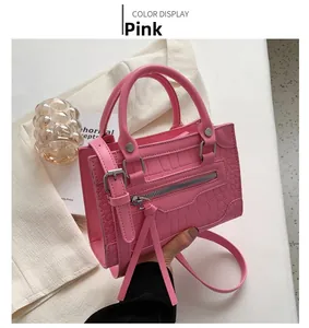 Macro view of pink crocodile-embossed leather handbag with metallic zipper and stud details
